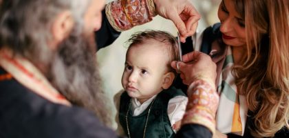 A baby's first haircut performed during a religious ritual with parents and clergy present.