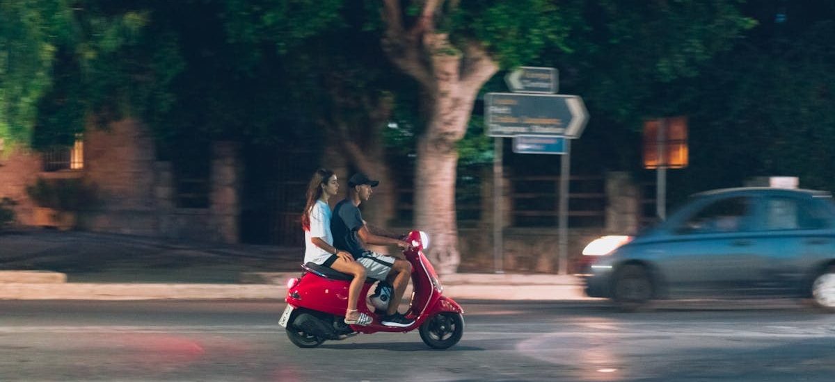 A couple rides a red scooter at night in Rodos, Greece, capturing a lively street scene.