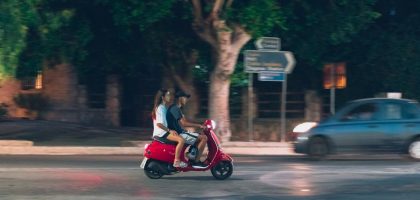 A couple rides a red scooter at night in Rodos, Greece, capturing a lively street scene.