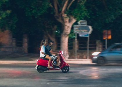 A couple rides a red scooter at night in Rodos, Greece, capturing a lively street scene.